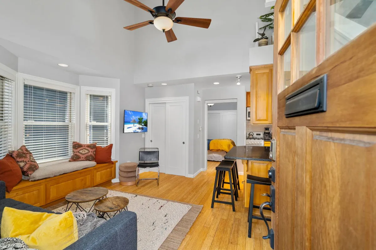 A cozy dining area adjacent to large windows, featuring a wooden dining table with comfortable seating and a soft seating area nearby. Natural light pours in, creating a bright and cheerful atmosphere ideal for sharing meals and conversation.