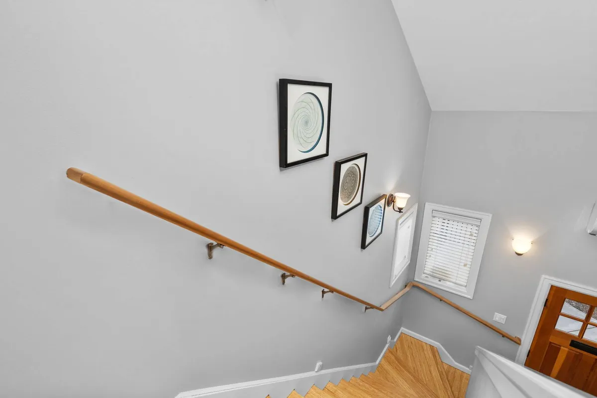 The image highlights an interior staircase framed by bright natural light and adorned with distinctive wall art. A modern handrail and stylish light fixture create an artistic, welcoming atmosphere, while the window casts inviting daylight across the landing.