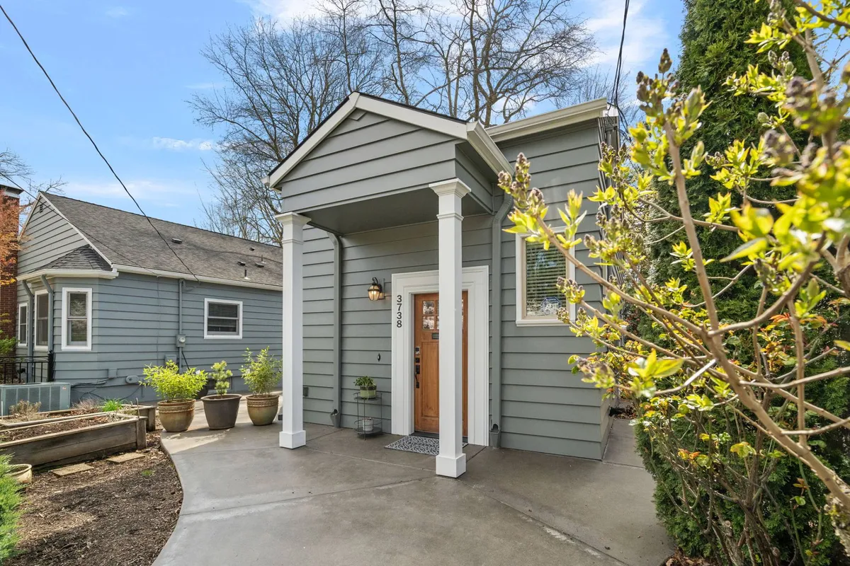 This exterior image features the home's welcoming front door, classic columns, and flourishing planters, set within a charming streetscape. The foreground hints at the vibrancy of the neighborhood, inviting residents and guests alike to step outside and begin their Laurelhurst explorations.