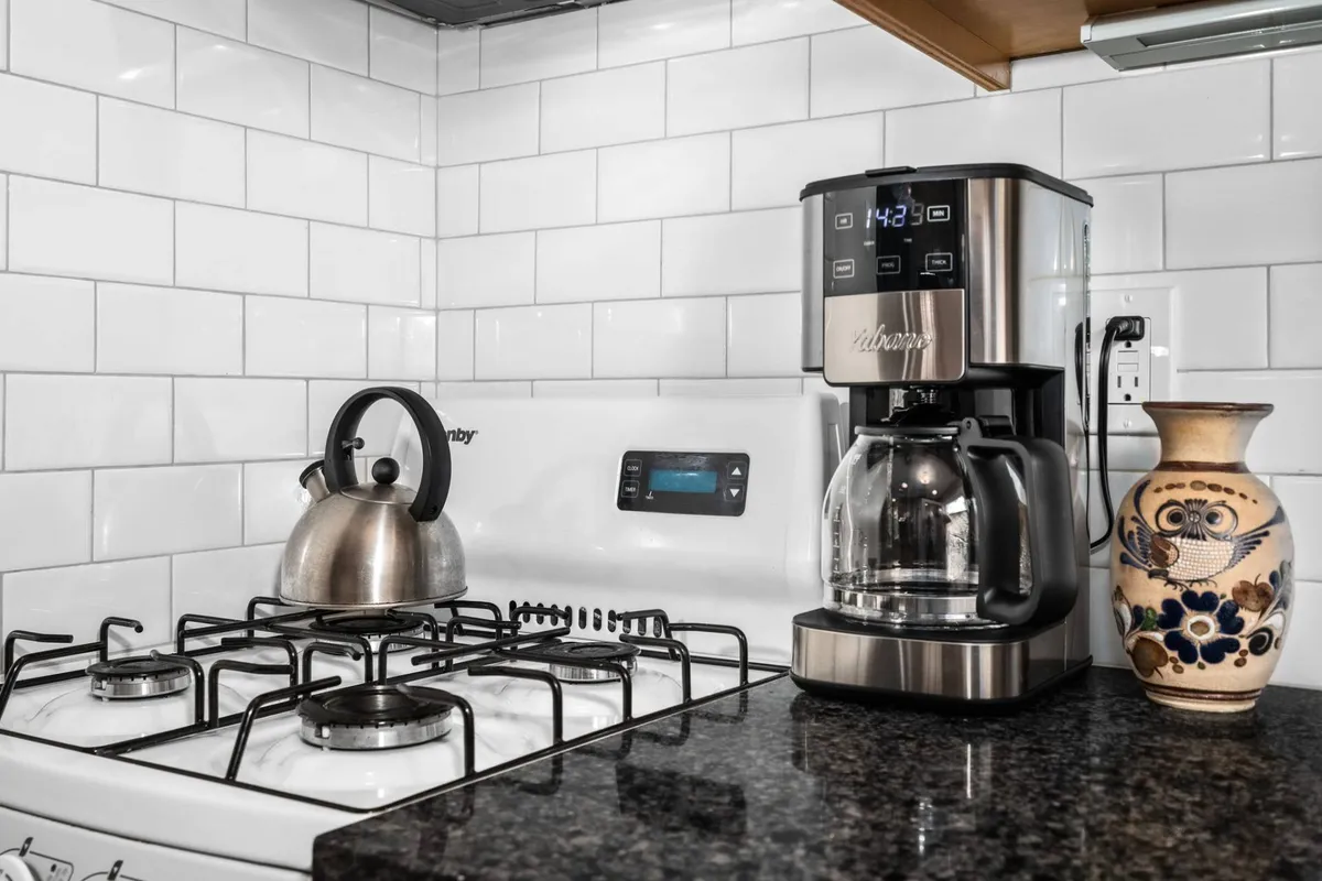 A modern kitchen space with a coffee maker, kettle, granite countertop, and a decorative vase. The area feels functional yet inviting, emphasizing daily comforts like brewing the first coffee of the day and gathering with family or friends.