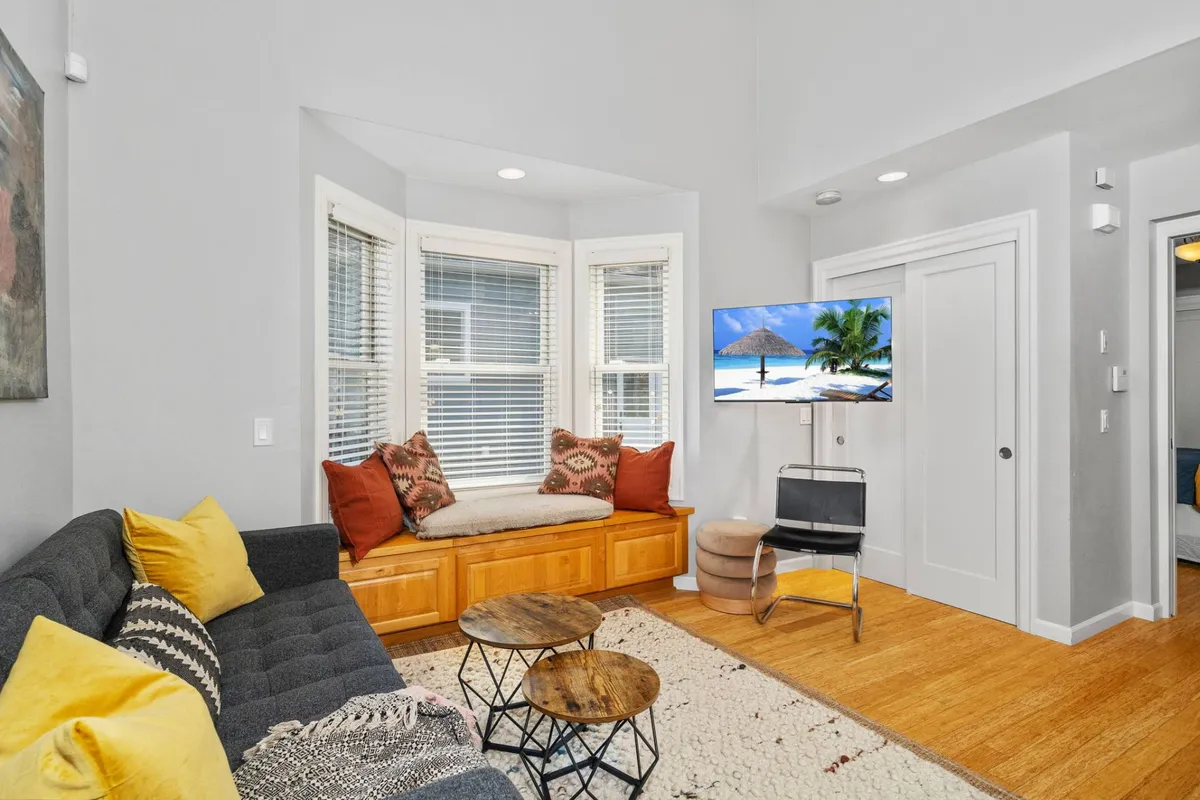 A cozy living room featuring a comfortable couch and a window seat, perfect for relaxing, reading, or enjoying a quiet evening. The television is positioned for movie nights, while soft lighting and homey decor create an inviting atmosphere.