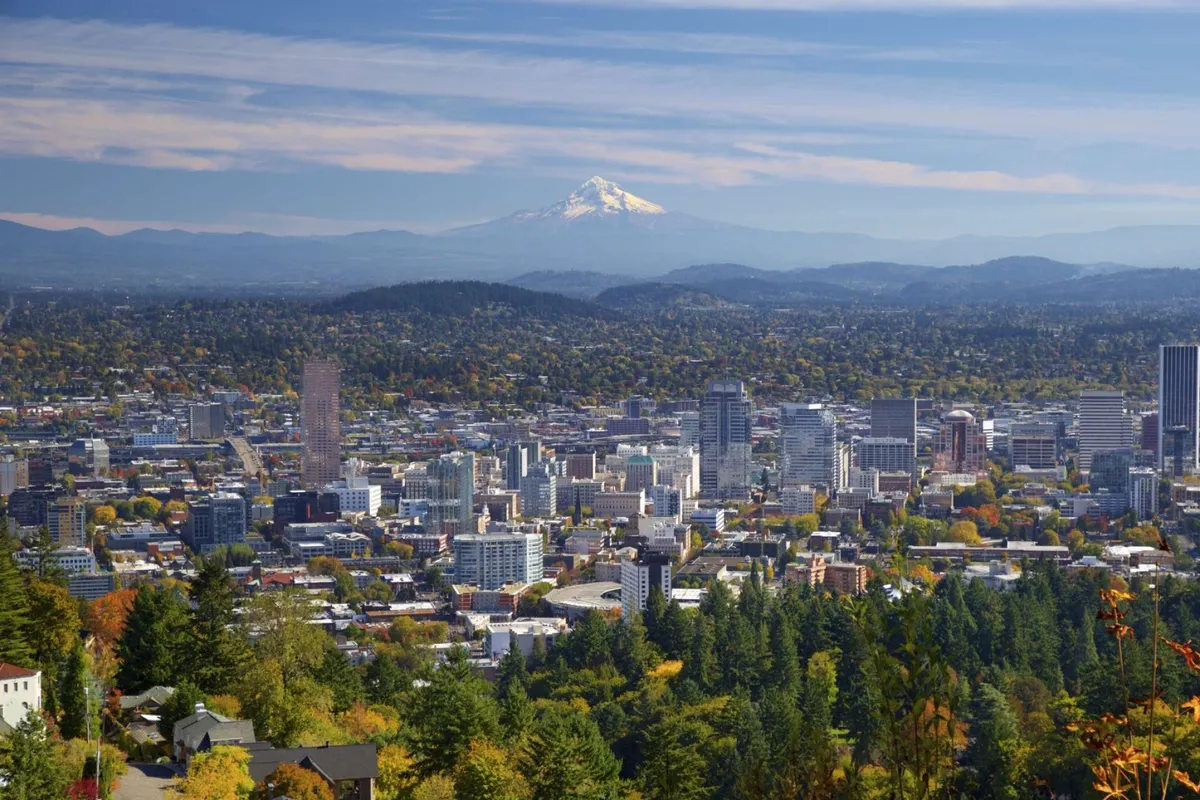 A panoramic view of Mount Hood rising behind downtown Portland, framed by lush greenery in the foreground. The image combines urban vibrancy with natural beauty, highlighting the city’s distinctive eco-minded character.