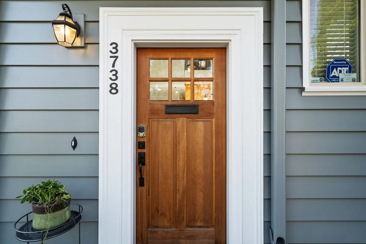 The image shows the home's inviting front entrance, featuring a prominent front door, clear house number, a welcoming lantern, and a lush planter. The setting hints at a warm first impression and the sense of homecoming that greets visitors and residents alike.