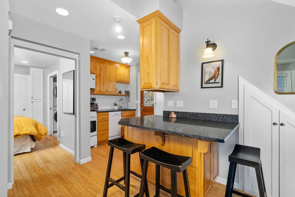 A welcoming kitchen scene featuring a granite countertop, wooden cabinets, bar stools, and visible modern appliances. The setup is designed for both casual dining and meal preparation, with cozy lighting and a layout that encourages social interaction and culinary creativity.
